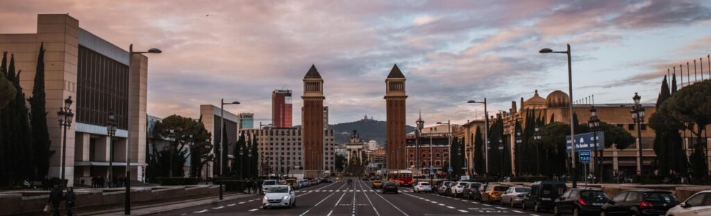Wide street view in Barcelona featuring the iconic Venetian Towers at sunset.